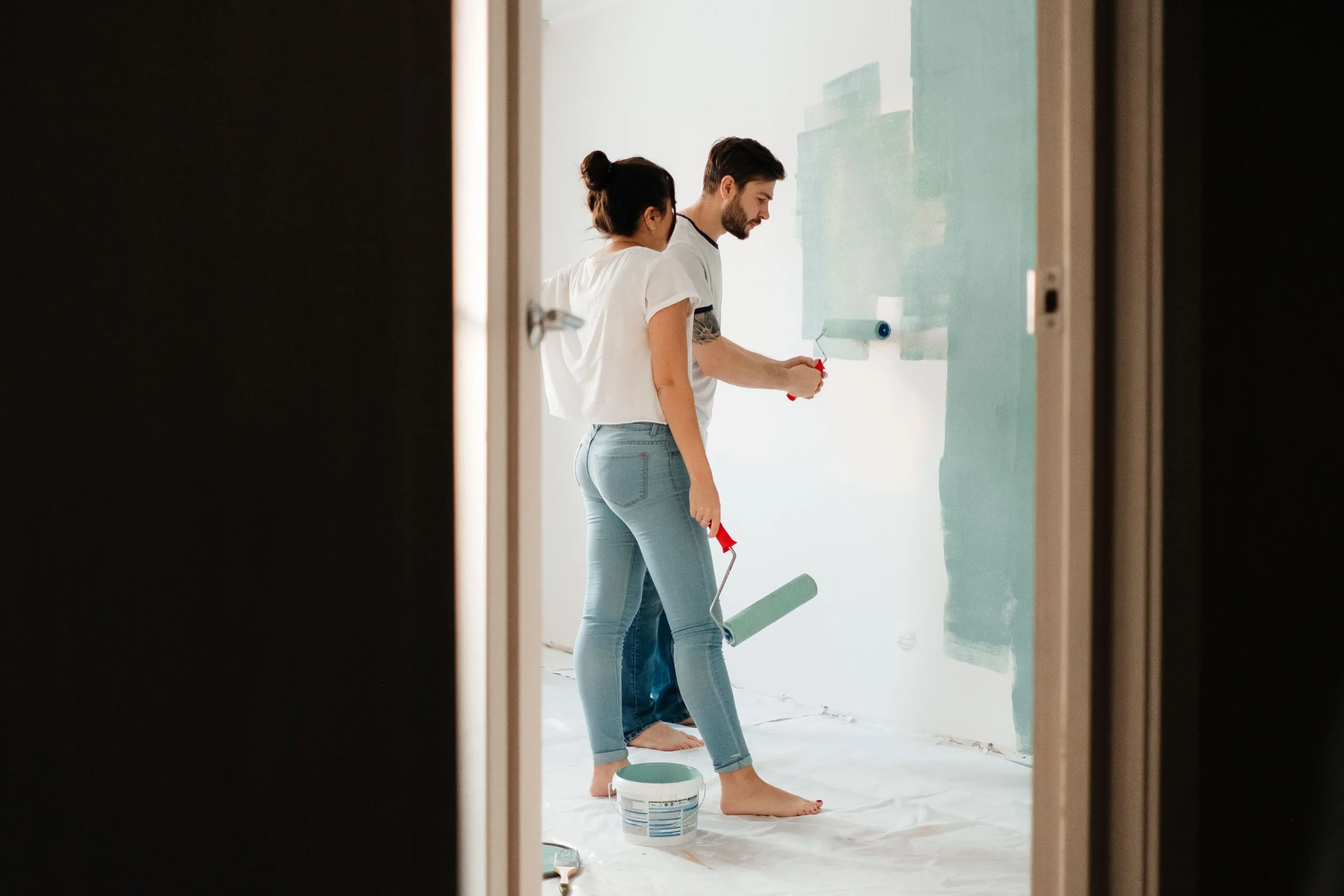 A man and woman painting a room wall with rollers, showcasing teamwork in home renovation projects.