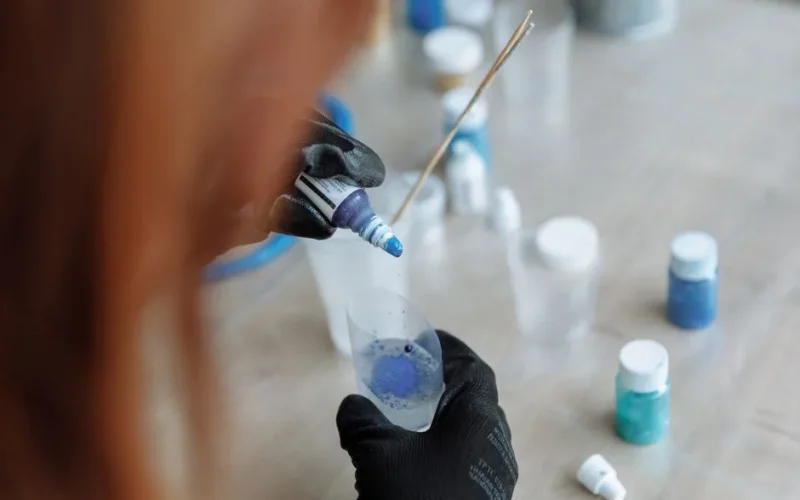 Detailed view of an artist using gloves to mix blue pigment in a vial for an art project.