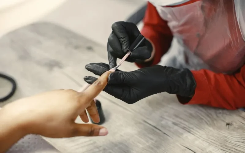 A nail artist carefully applies nail polish to a client's nails in a salon setting, using precise techniques.