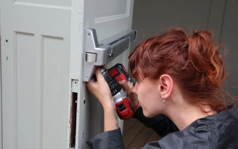 Caucasian woman focusing on door installation with power drill, side view.
