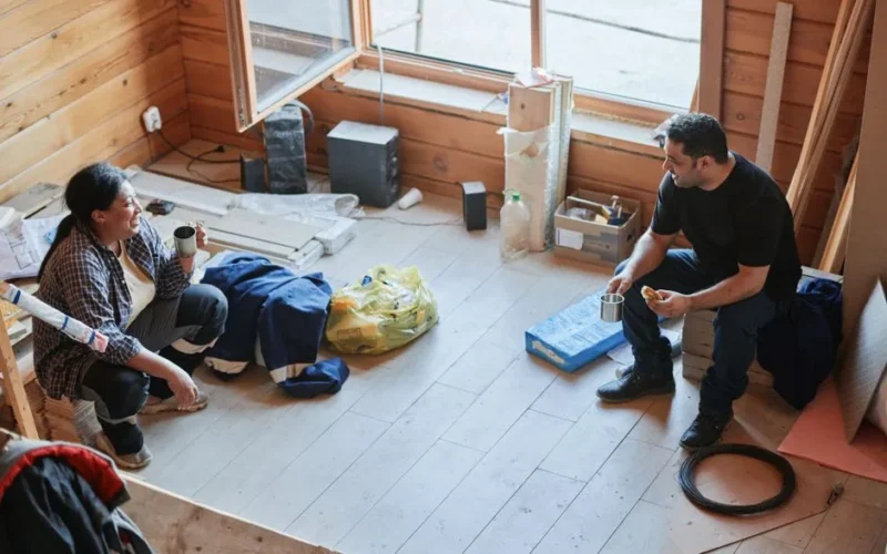 Two construction workers taking a break and chatting inside a wooden room during a renovation project.