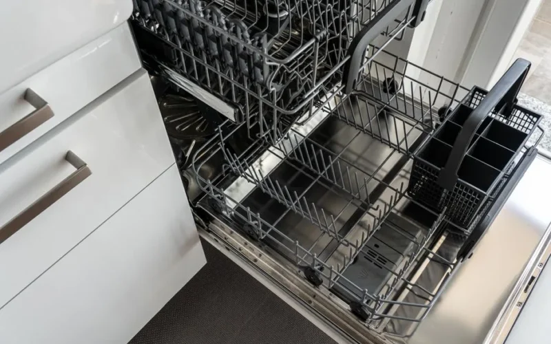 A clean and empty stainless steel dishwasher open in a modern kitchen setting.