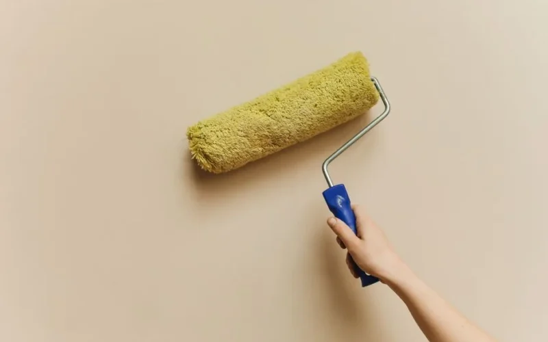 A hand using a yellow paint roller to paint a beige wall. Perfect for DIY and home improvement themes.