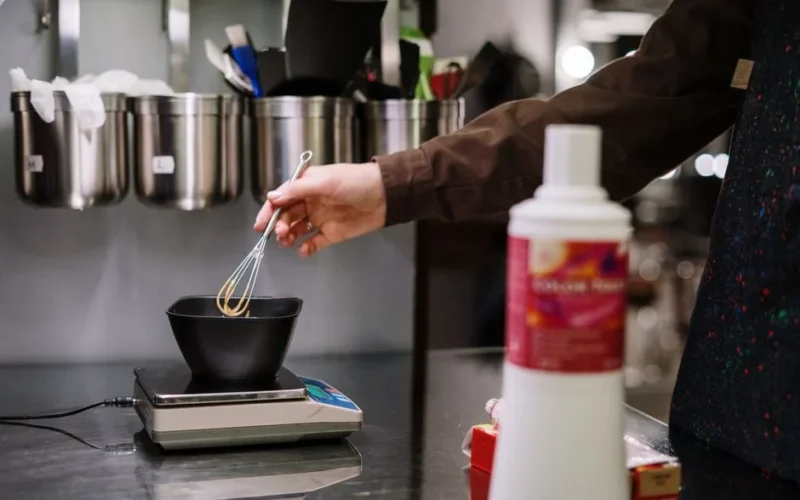 A stylist prepares hair dye with precision using professional tools in a salon setting.