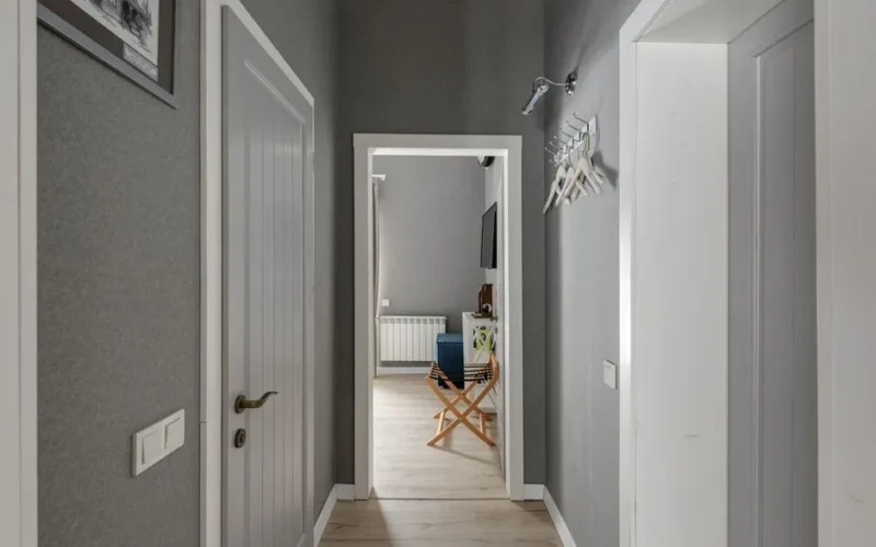 Spacious hallway with grey walls, wooden doors and white hangers, leading into a modern room.