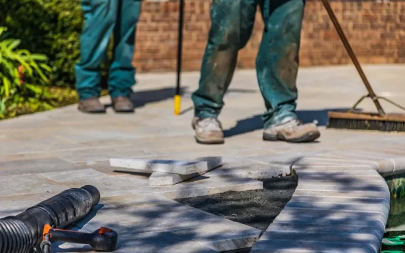 Workers laying tiles on an outdoor patio under sunlight.