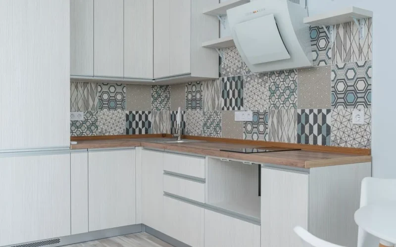 Interior of contemporary kitchen with white cabinets and wooden counter near ornamental tile on wall and modern appliances in apartment