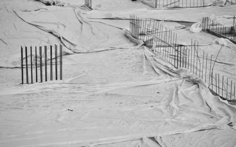 Monochrome image of a construction site with foundations covered by sheets and exposed rebar.