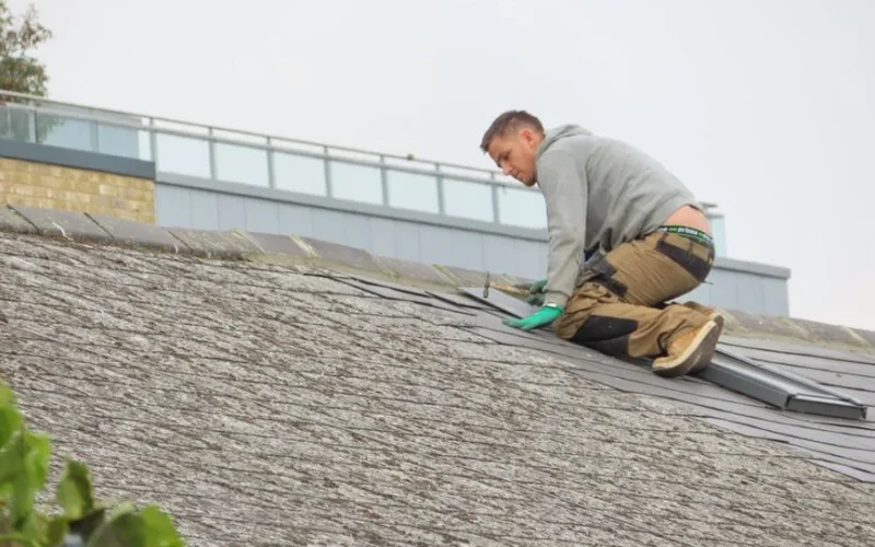 Construction worker installing shingles on a rooftop. Outdoor building maintenance.