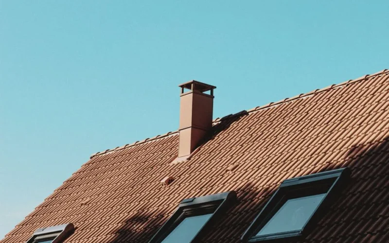From below of chimney and attic windows on tiled roof of modern residential house against cloudless blue sky