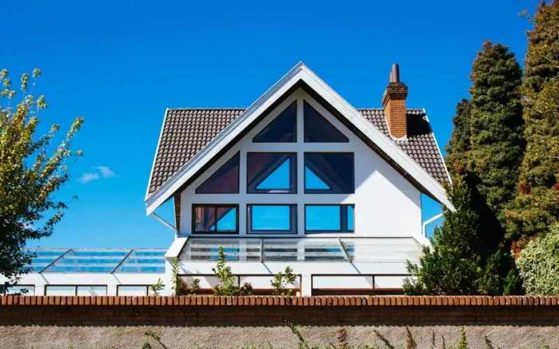 Contemporary A-frame house with large glass windows on a sunny day, surrounded by greenery.
