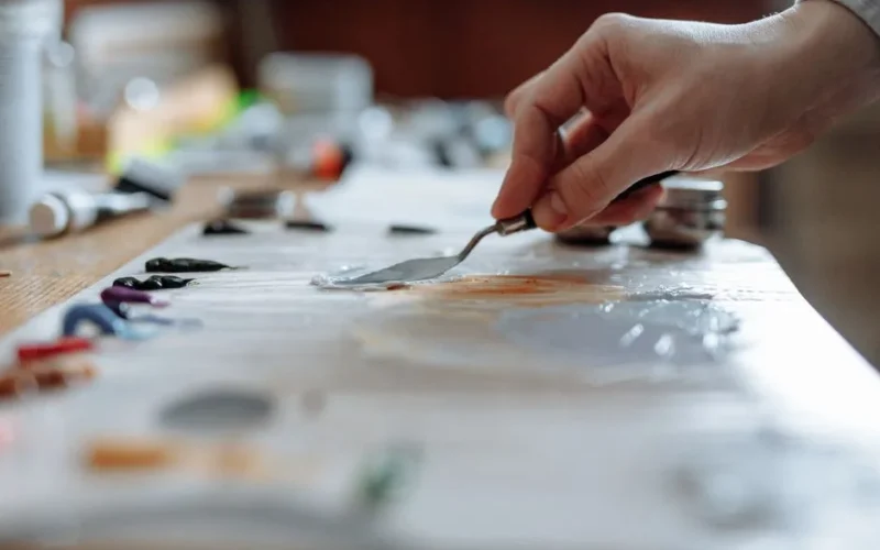Hand mixing vibrant oil paints on a wooden palette in an art studio.