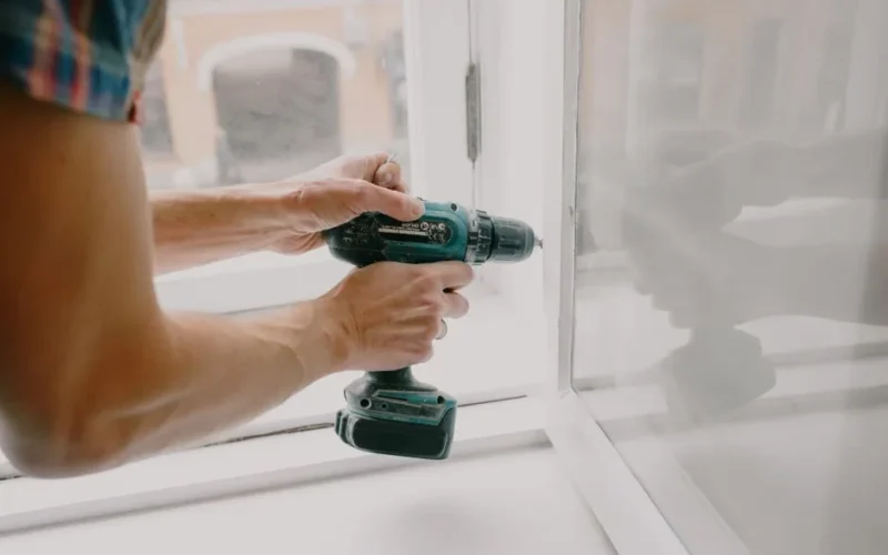Side view of crop anonymous male mechanic fixing window with screwdriver during renovation process in apartment