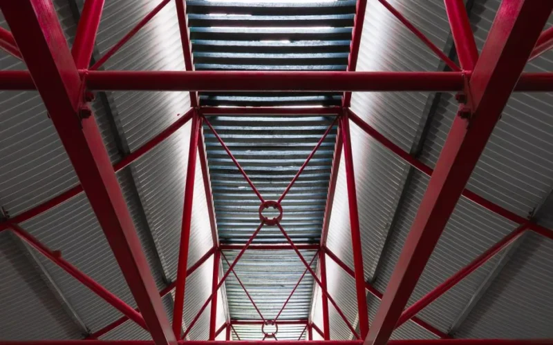 View of a steel roof supported by red beams in an industrial setting, emphasizing structure.