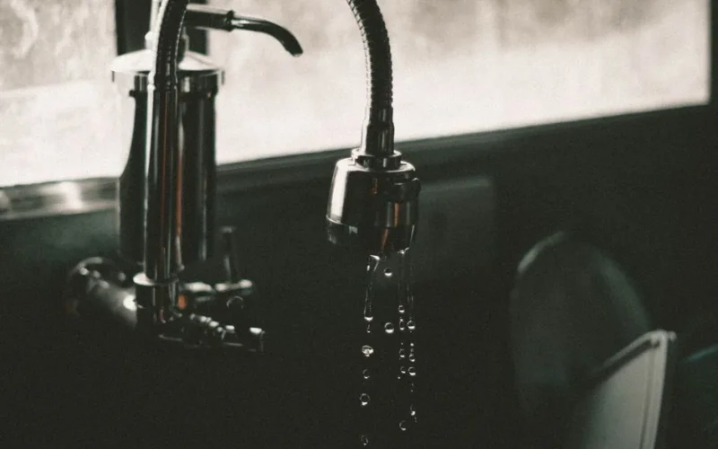 Close-up of a kitchen faucet with water droplets falling into the sink, captured in a minimalist style.