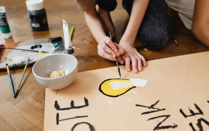 A student is painting a lightbulb for a school art project, focusing on creativity and expression.