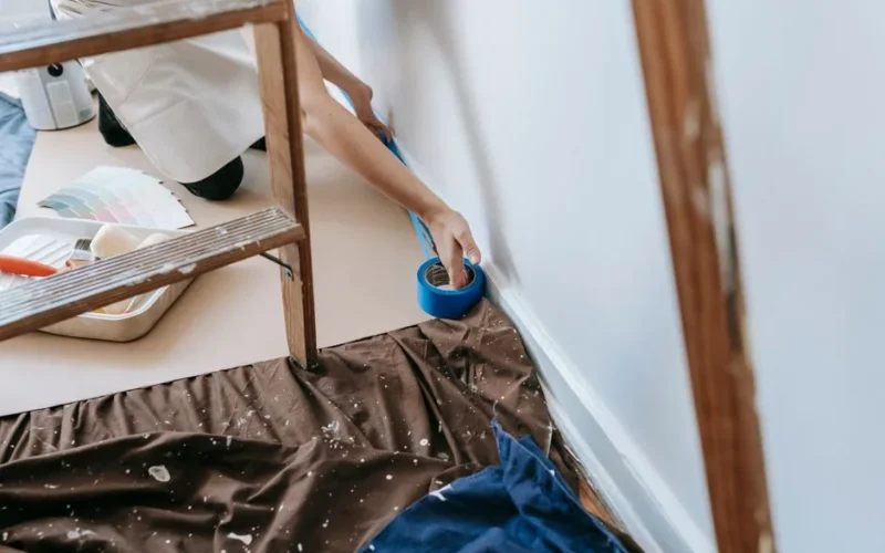 Woman preparing room for painting with adhesive tape and tools; home renovation project.