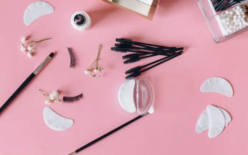 Aesthetic makeup tools and beauty items arranged on a pink surface.