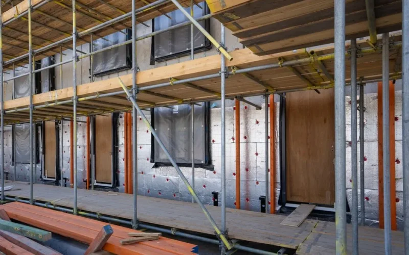 Scaffolding at a residential building under construction with windows and insulation sheets visible.