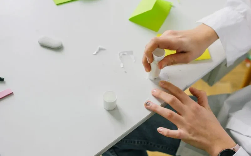 Close-up of hands applying glue stick on paper for a craft project on a desk.