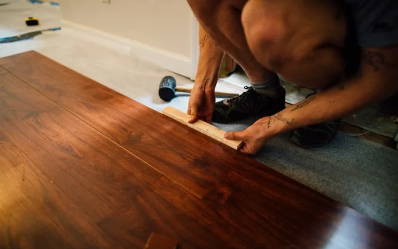 Faceless male master laying wooden laminate flooring using mallet in apartment during renovation