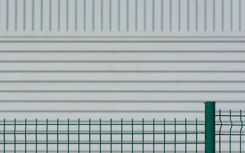 Green metal fence contrasts with a white corrugated wall, creating a minimalist pattern.