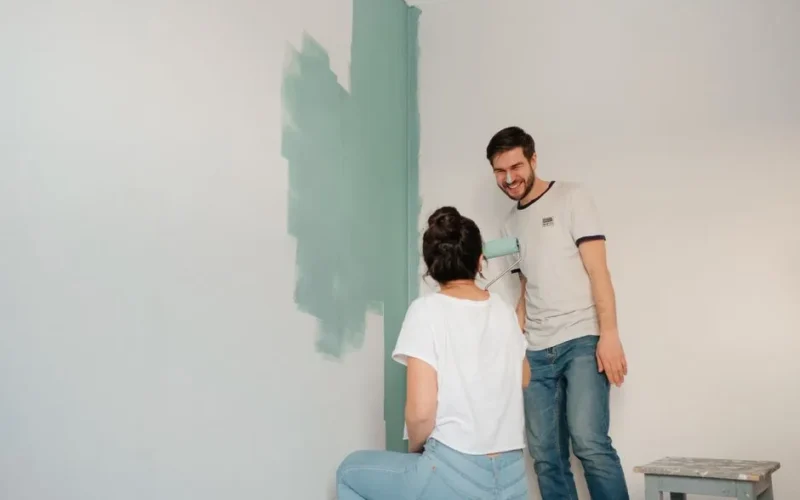 A couple laughing and enjoying painting a room together with a teal color.