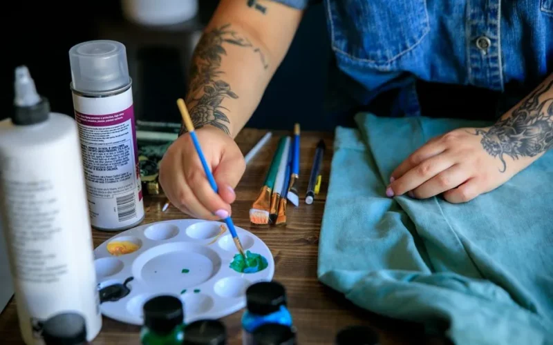 Close-up of a woman painting with diverse paints on a table, focusing on artistic creation.