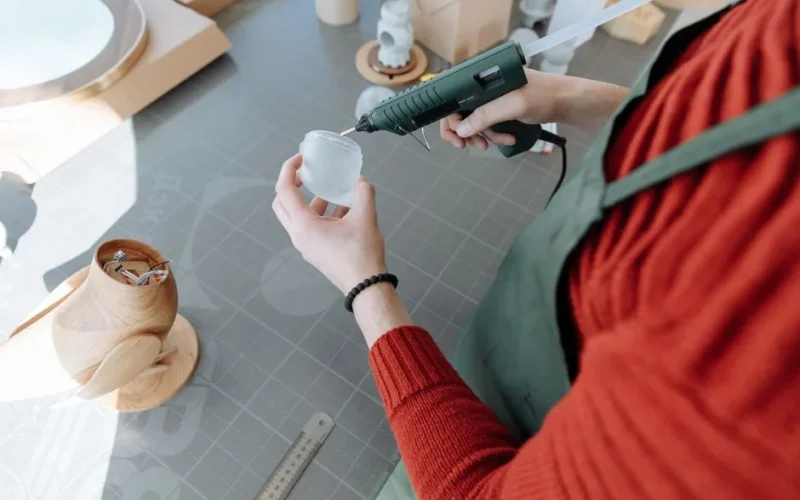 Handmade figurine assembly using a glue gun in a well-lit workshop environment.