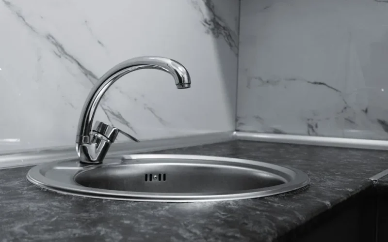 Stainless steel kitchen sink and faucet against marble backsplash in a modern kitchen.