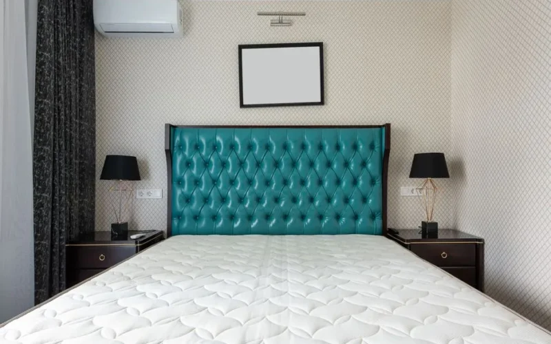 Mattress on bed with upholstery between lamps on bedside tables under air conditioning in house