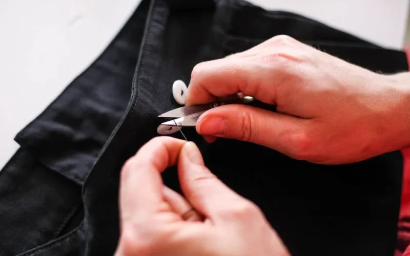 Close-up view of hands sewing black fabric with scissors, showcasing precision stitching.