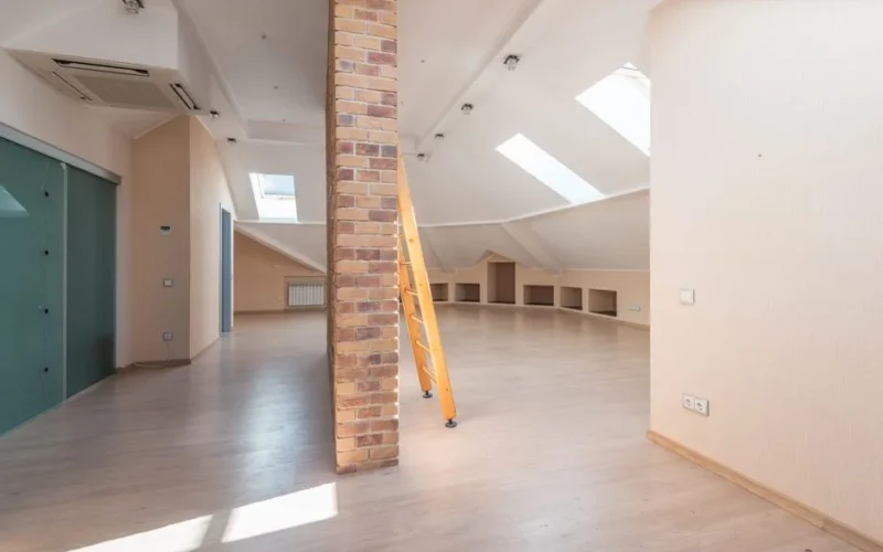 Spacious attic room with natural light from skylights, featuring a brick pillar and a wooden ladder.