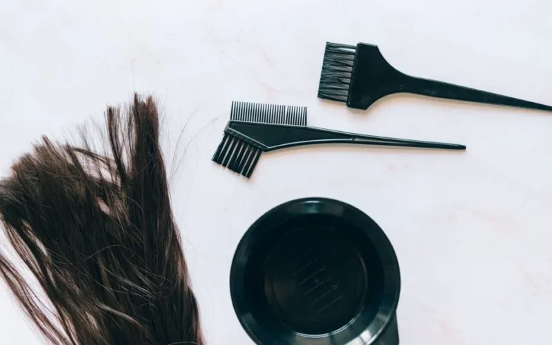 Top view of hair coloring tools and hair strands on a white background.