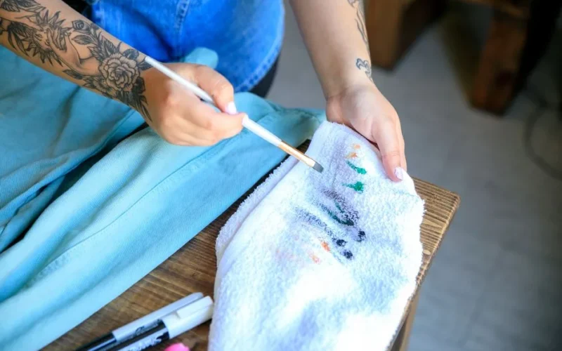 Close-up of tattooed hands cleaning paintbrush on a towel, showcasing artistry and creativity.