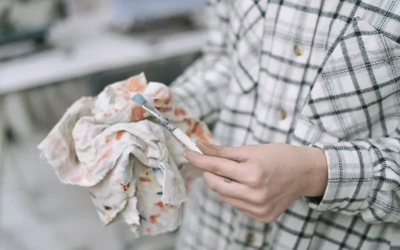 Close-up image of an artist in plaid shirt cleaning a paintbrush with a colorful cloth