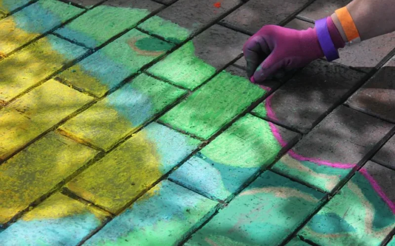 A vibrant chalk drawing on a Kansas City sidewalk with an artist's hand in colorful gloves.