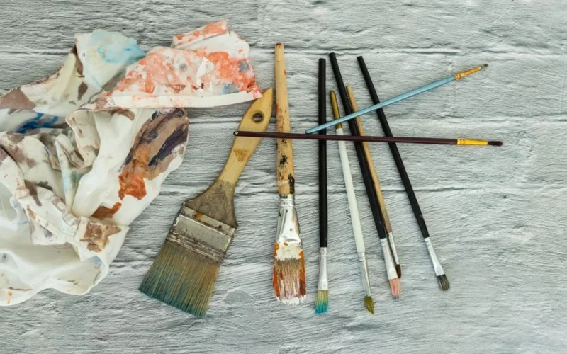 A collection of used paintbrushes and a colorful palette resting on a textured surface, ideal for art themes.