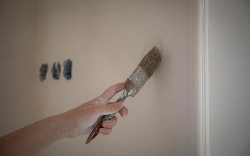 Close-up image of a hand painting a wall with a brush for home renovation.