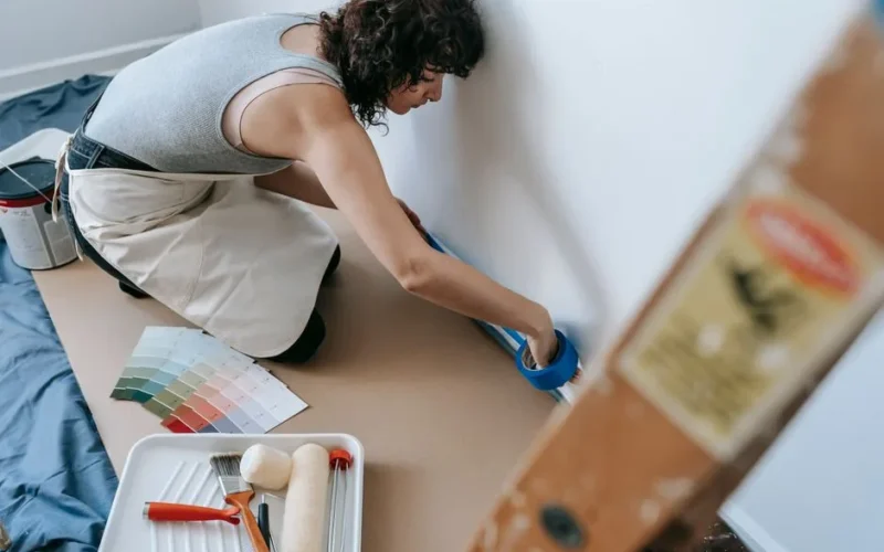 Female using blue tape for home painting project in a modern apartment.