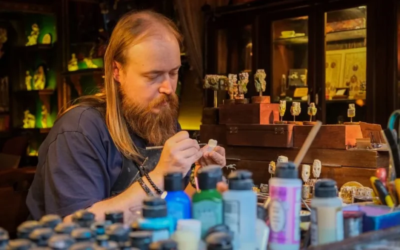 Skilled artisan meticulously painting miniatures in a cozy, cluttered workshop with various vibrant paints.