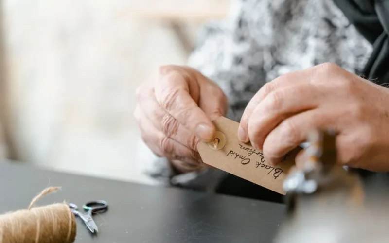 Detailed view of hands attaching a handmade gift tag with jute string, emphasizing craftsmanship.
