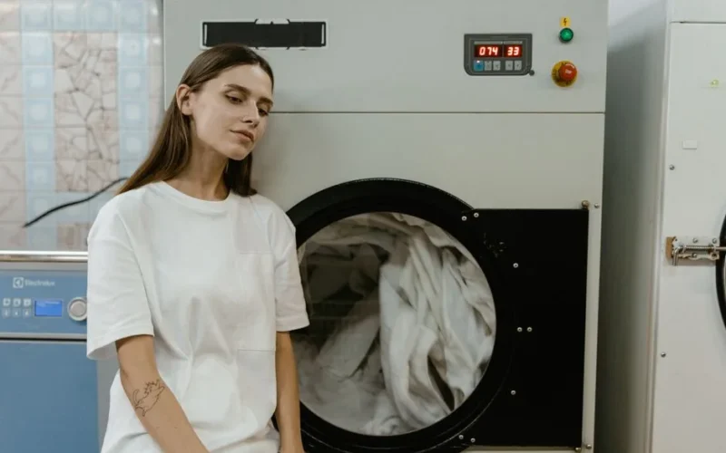A woman in a laundry facility standing by a washing machine, contemplating the process.