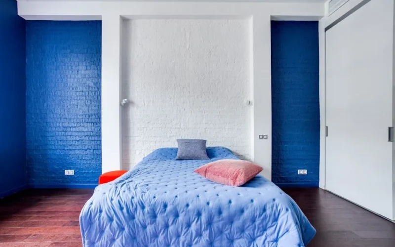 Modern bedroom with navy blue walls, cozy bed, and stylish pillows.