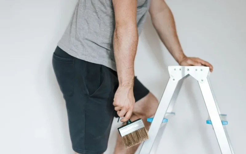 Side view of crop anonymous male decorator in casual clothes preparing to painting walls of light room while standing on stepladder