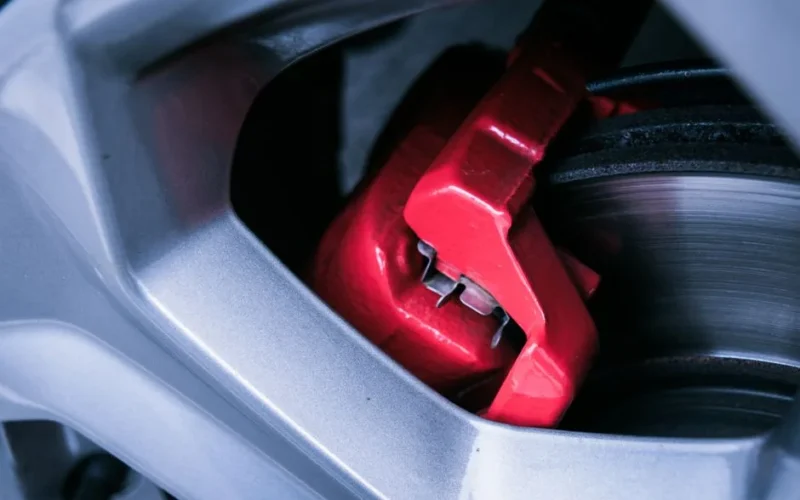 Detailed photo of a red automotive brake caliper and disc brake in focus.