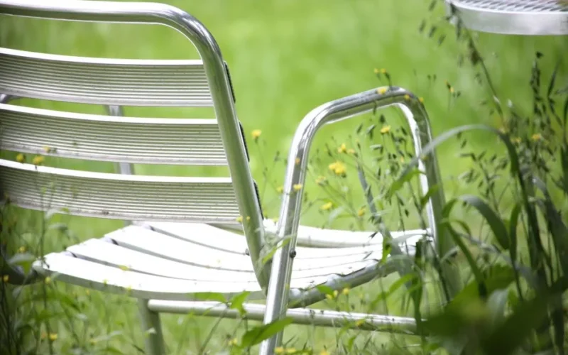 Empty metal chair surrounded by lush greenery and wildflowers in a tranquil garden.