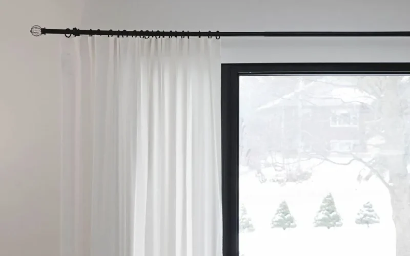 White curtains partially covering a window with a snowy outdoor view. Minimalist home decor.