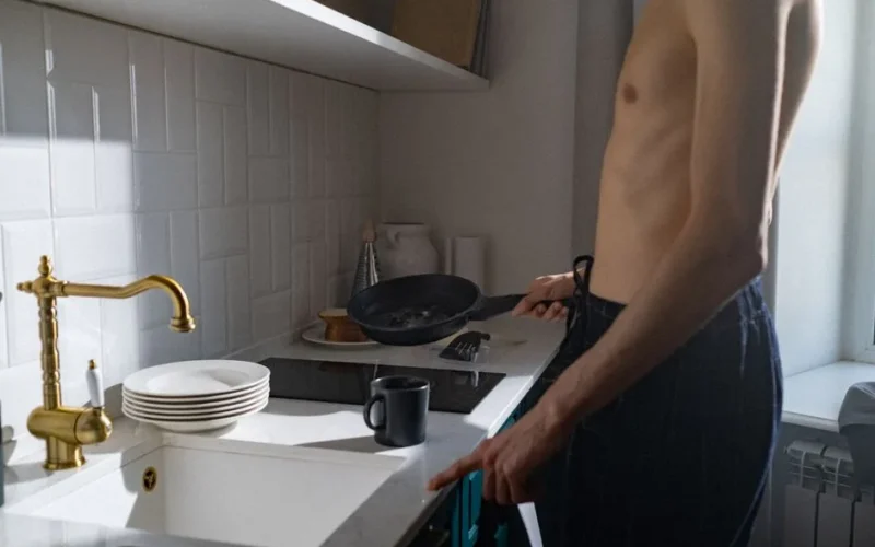 A young man prepares breakfast in a sunlit kitchen, capturing a daily routine moment.