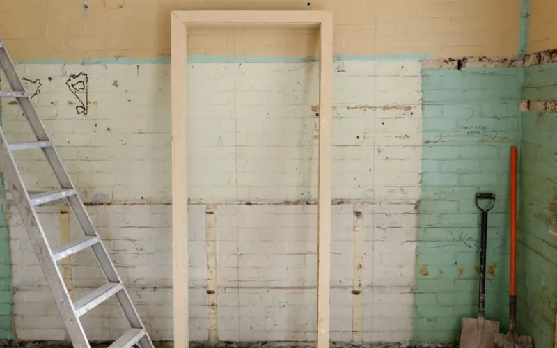 Renovation scene featuring ladder, frame, and tools against partially demolished walls.